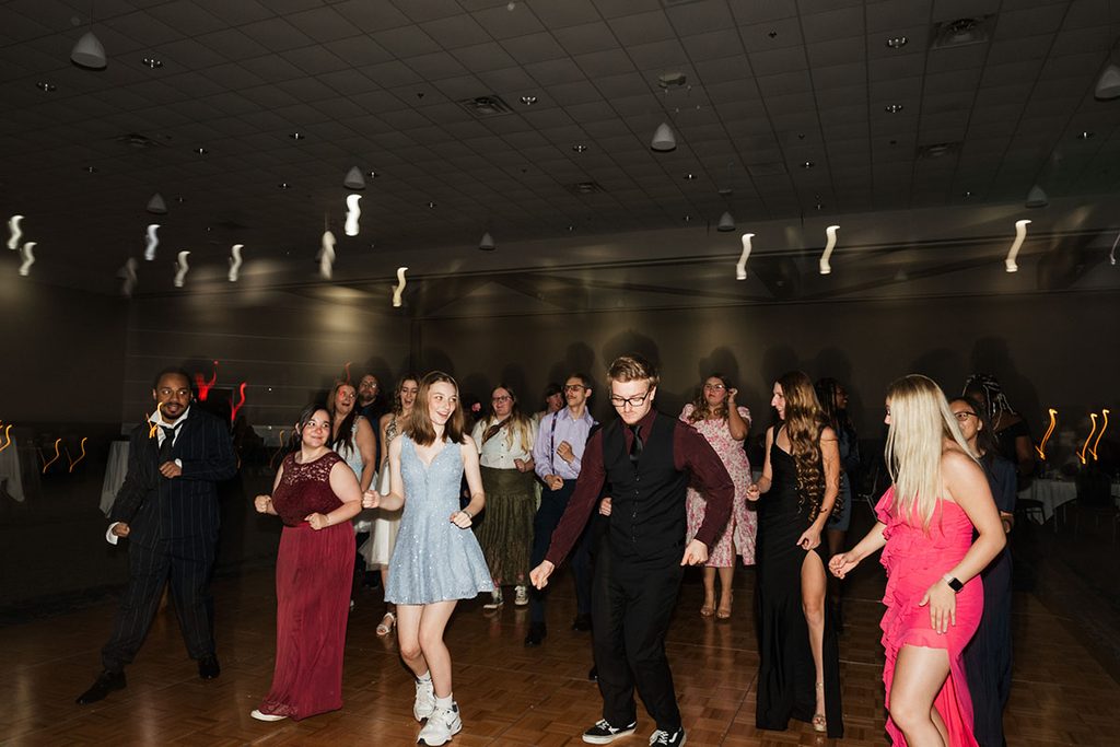 A group of people dance together in a dimly lit venue, showcasing a variety of formal attire.