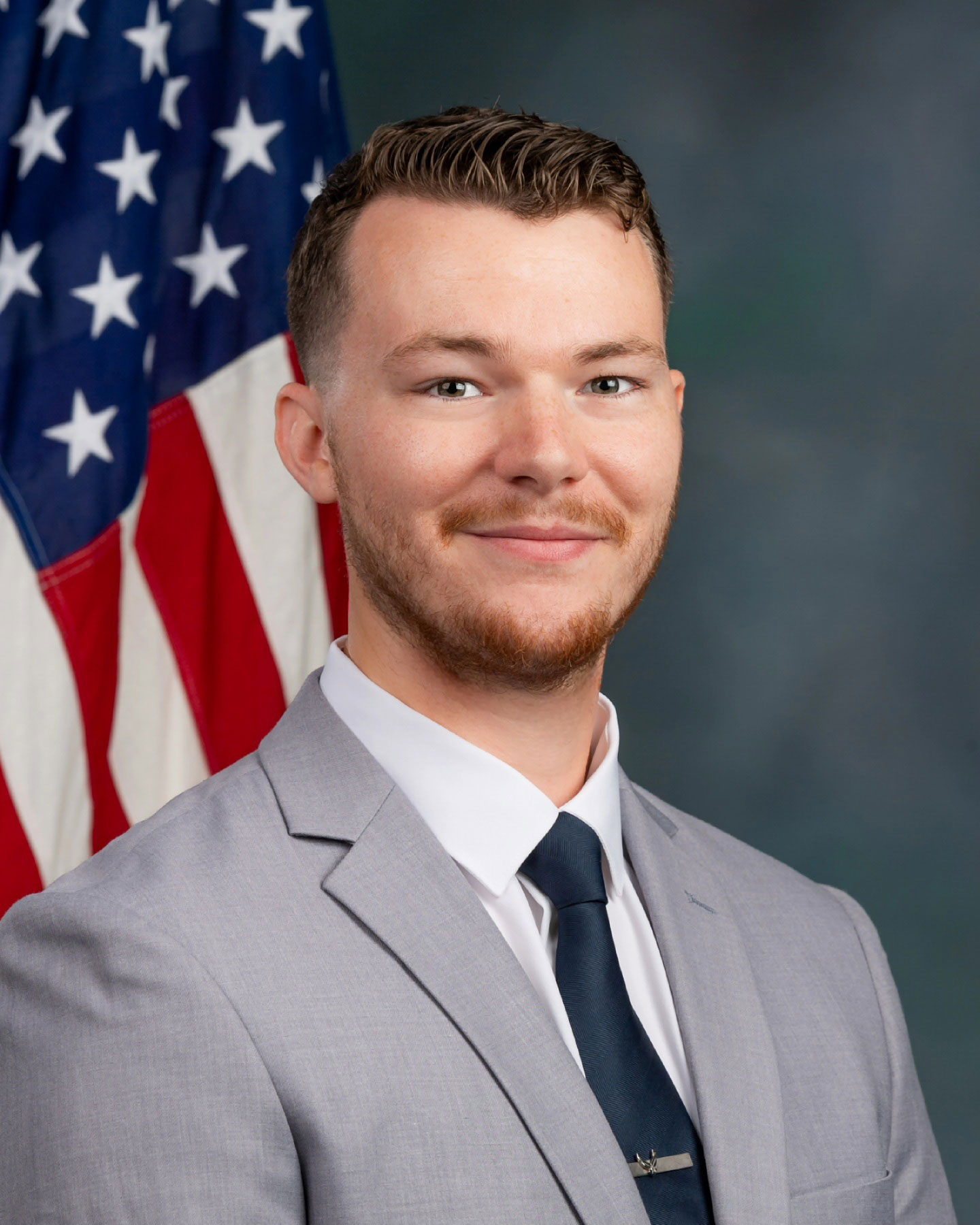 Dallas Watkins in a suit smiles in front of an American flag backdrop.